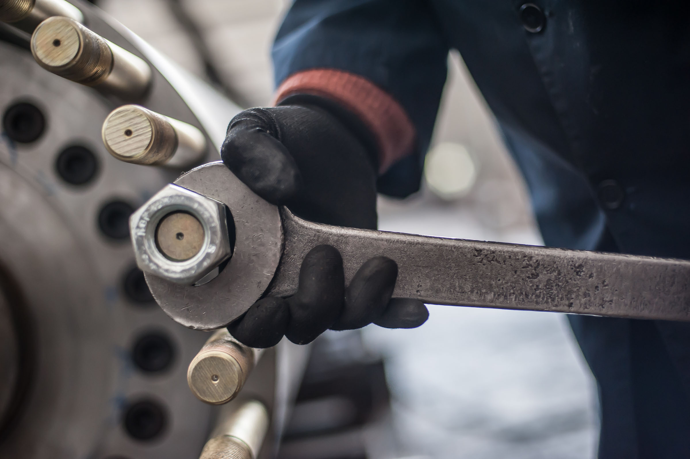 Mechaniker in der Fabrik schraubt großen Bolzen mit großem und schwerem Schraubenschlüssel und hält ihn mit beiden Händen